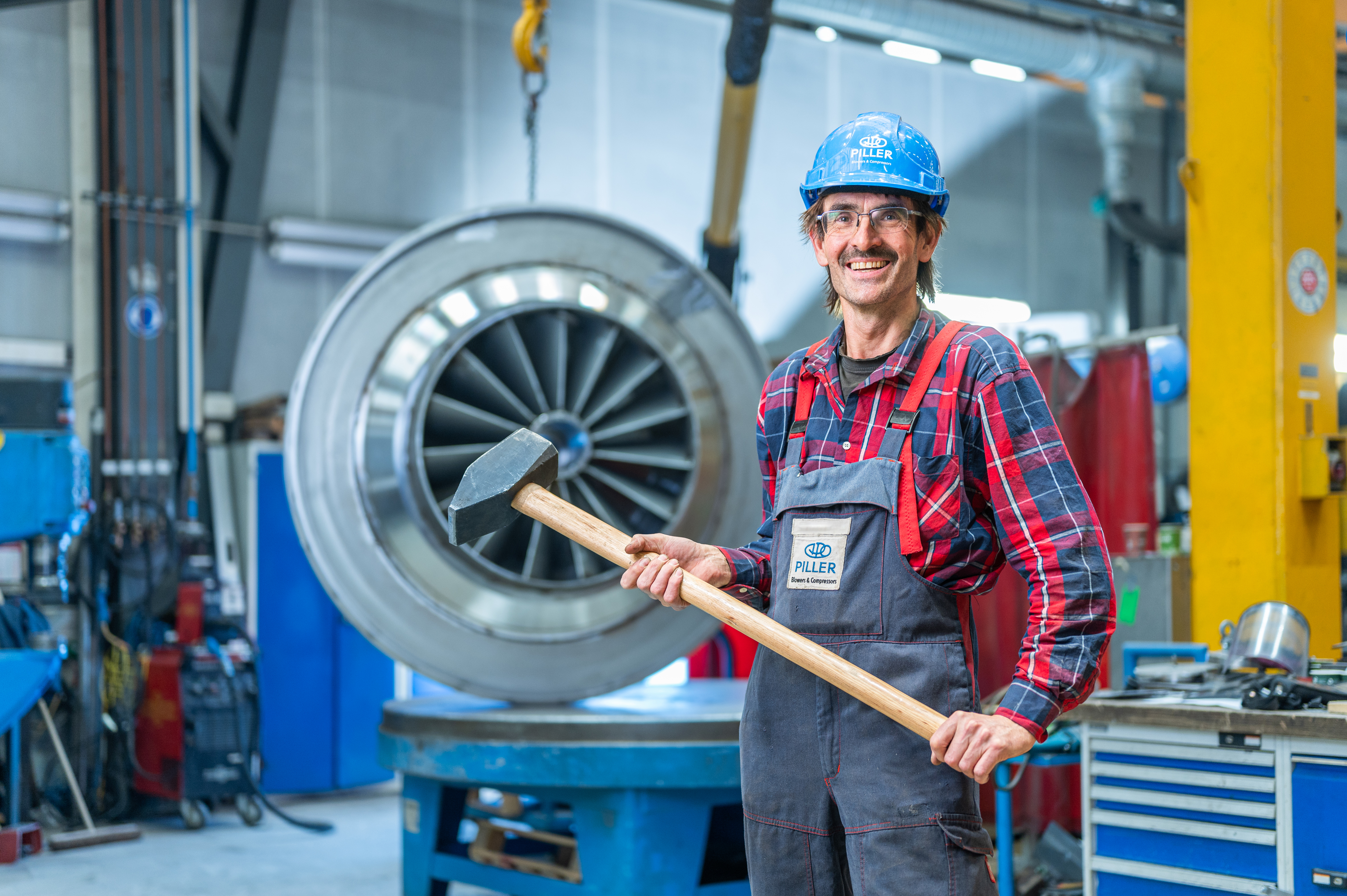 Piller-Mitarbeiter mit Schutzhelm und Hammer vor Turbine in Werkshalle