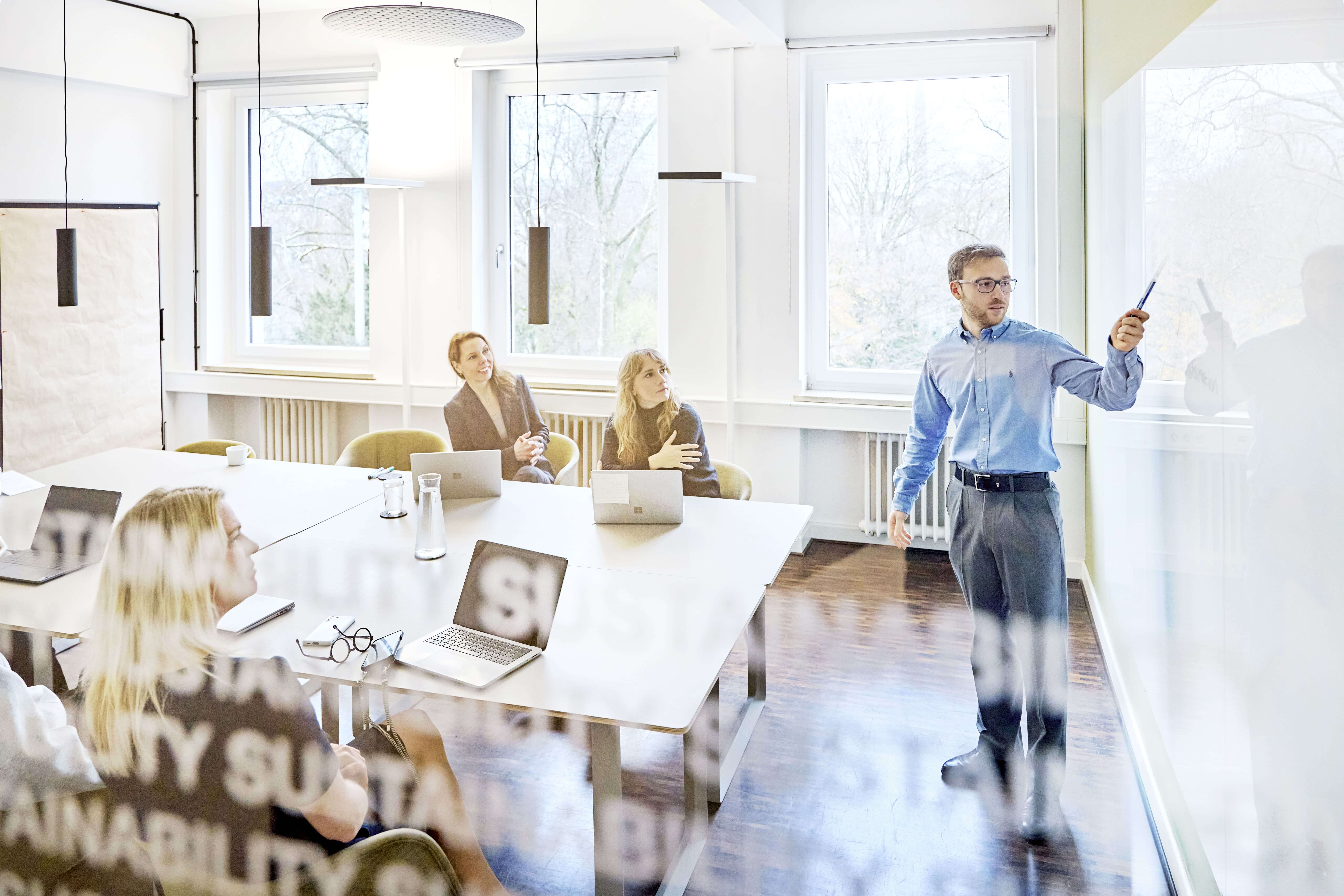 Mitarbeiter erklärt seinen Kolleg:innen etwas an einem Whiteboard.