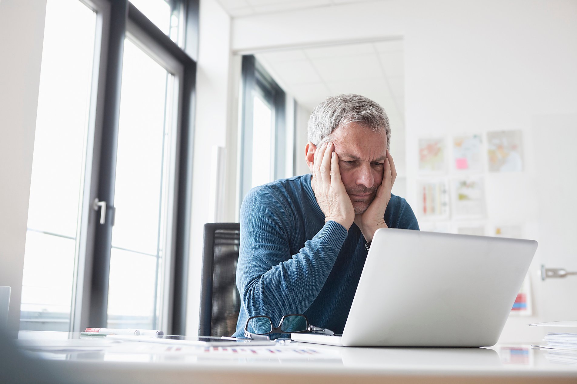 Mann sitzt im Büro nachdenklich vor seinem Laptop